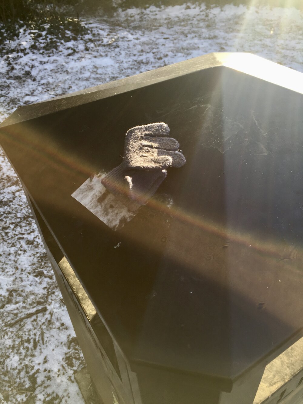  A single glove is atop a black bin. It shines in a beam of winter sun. 