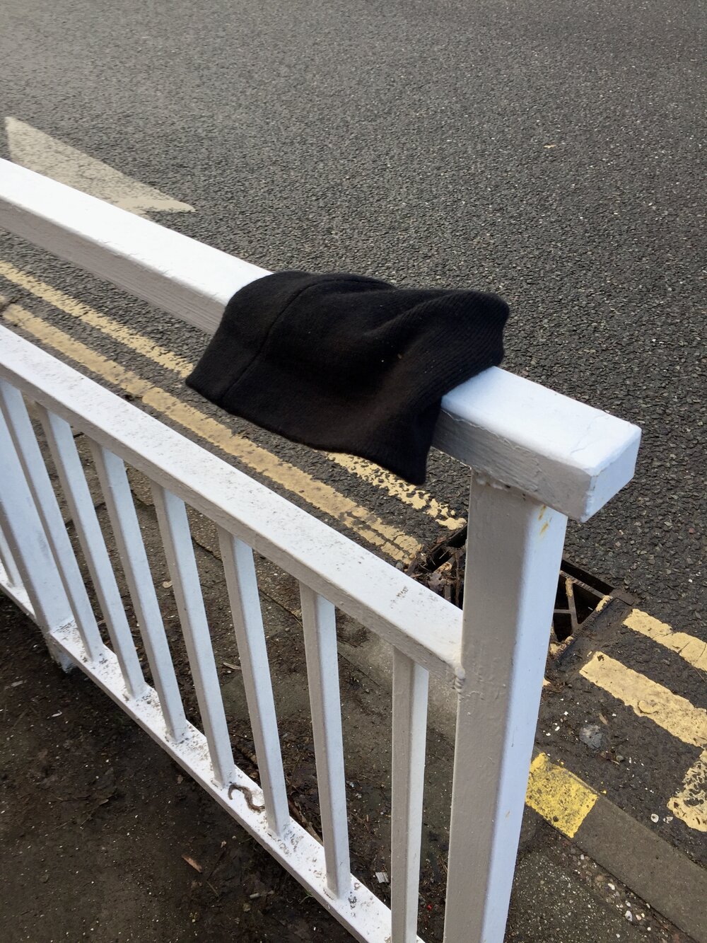  A black beanie hat flops over a white railing next to a road. 