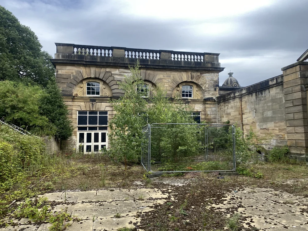  The Experimental Theatre studio. The giant mask is here, on the right, half-hidden by saplings. The clock of the Stable Block is visible behind. 