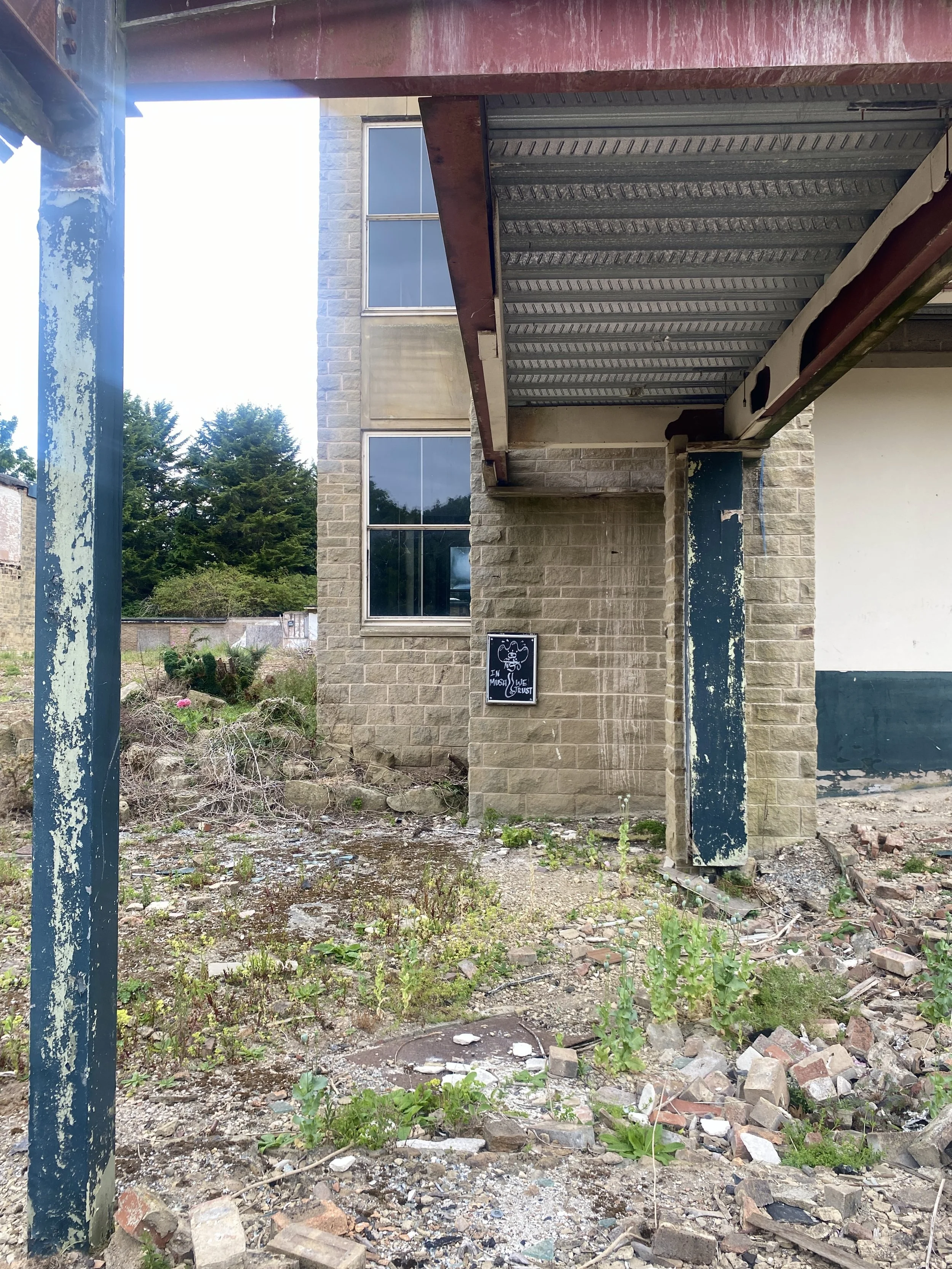  The east side of the Sir Alec Clegg Building, with a walkway going to nowhere above, and a sign saying, “IN MUSH WE TRUST”. 
