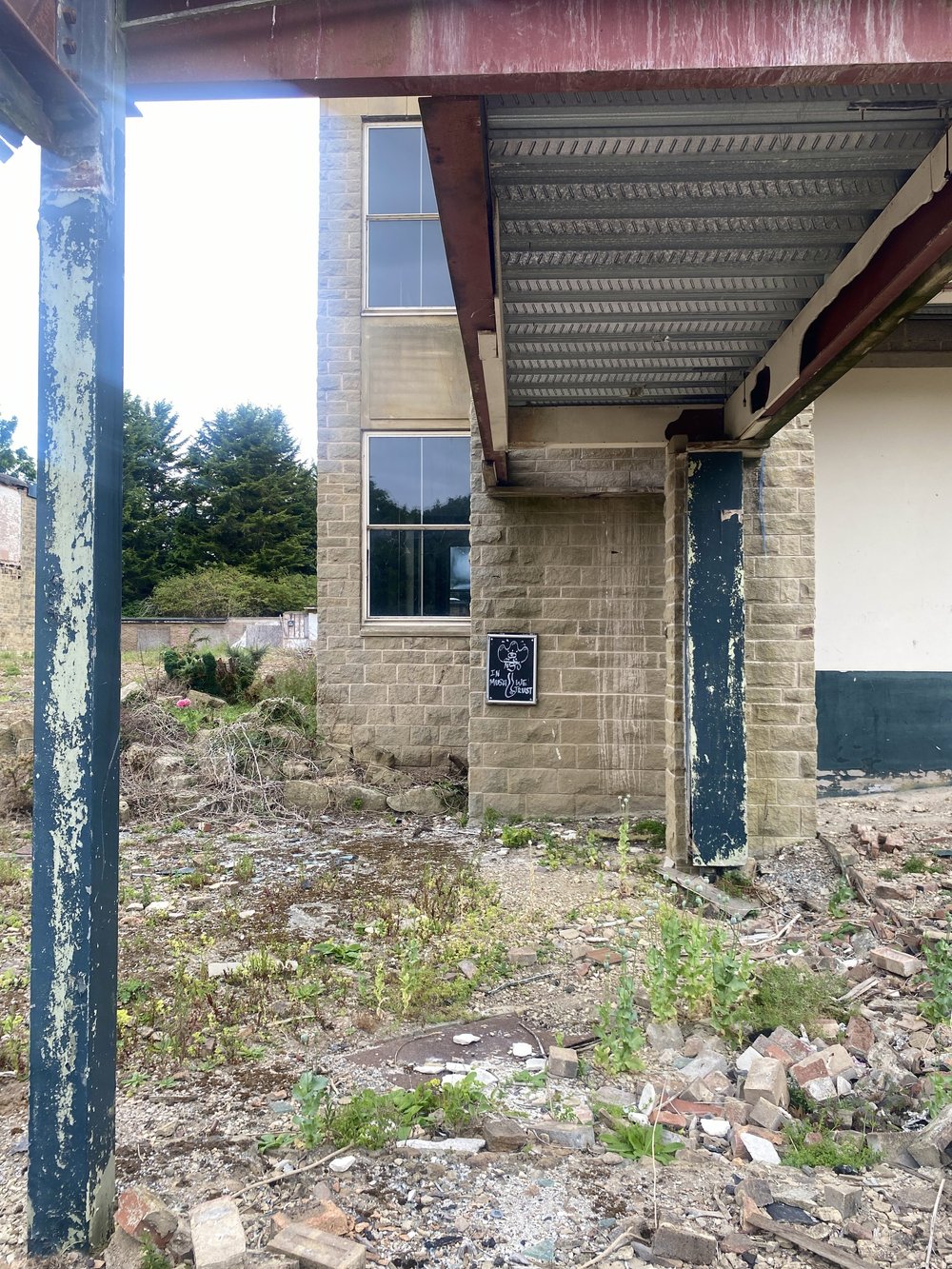  The east side of the Sir Alec Clegg Building, with a walkway to nowhere above, and a sign saying, “IN MUSH WE TRUST”. 