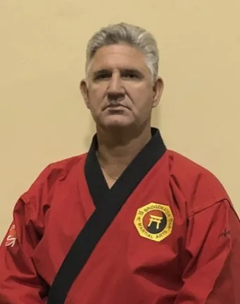Man in a red martial arts uniform with black trim, standing against a yellow wall.
