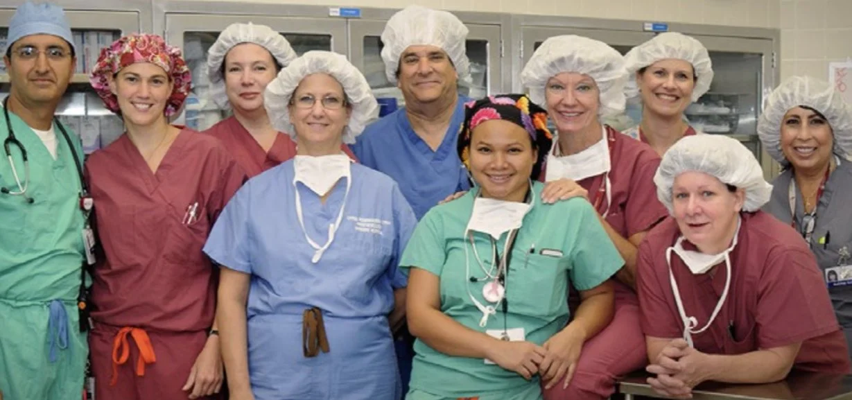 Group of healthcare professionals wearing scrubs, surgical caps, and masks in a hospital setting.