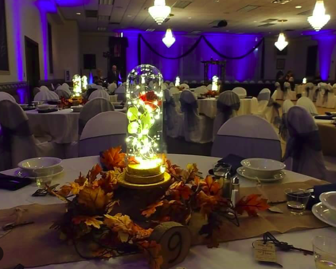 Elegant banquet hall with round tables decorated with autumn leaves, illuminated centerpieces, and table settings, ready for a celebration or event.
