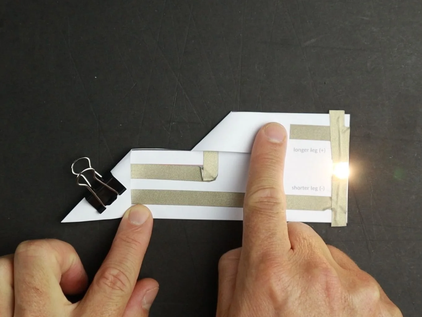 The finished Easy Circuit template with a light up LED and a finger pressing down on the DIY fold-over switch.