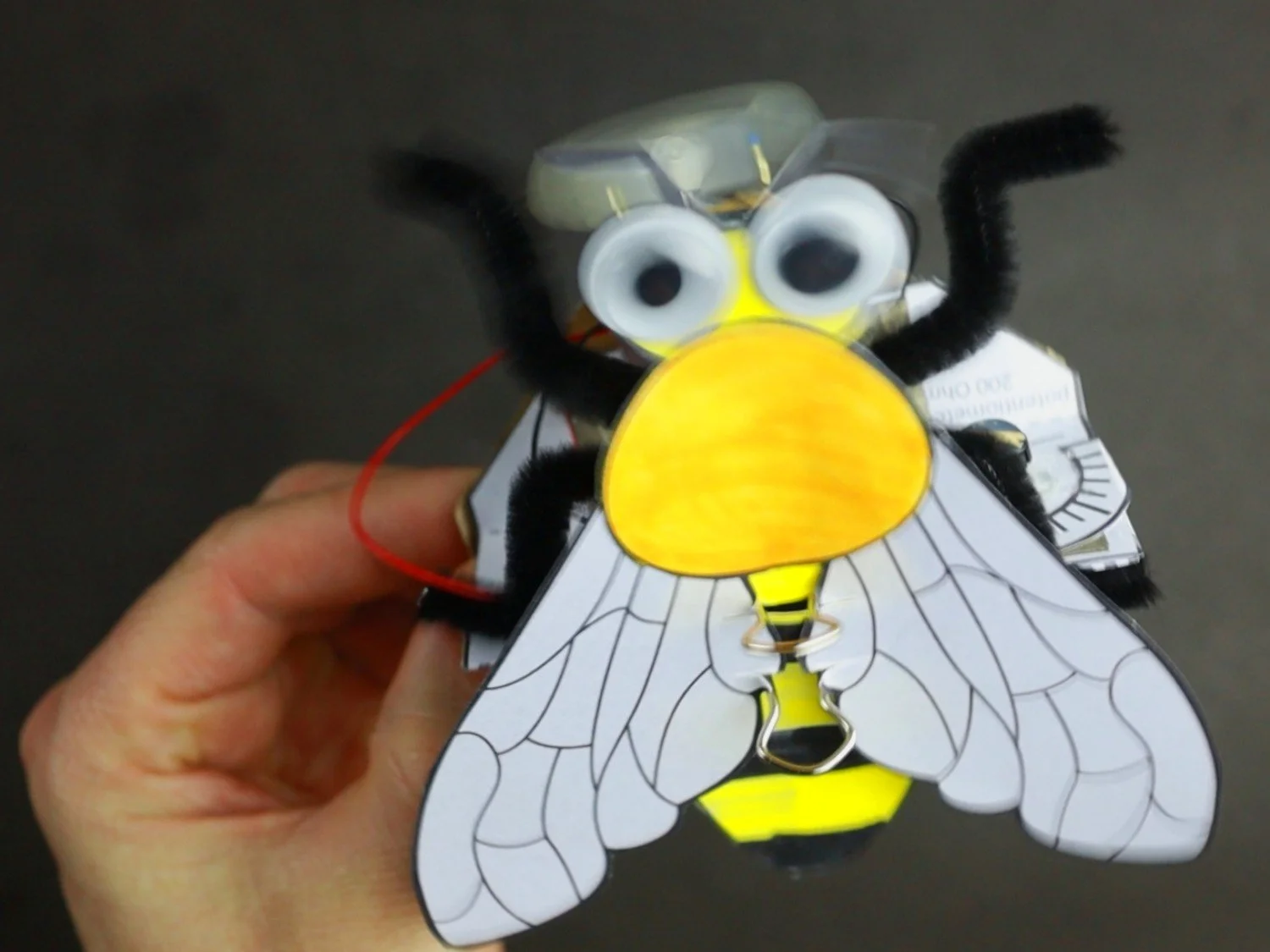 A picture of the BeeBot. A variation of the classic bristlebot. It is held up close to the camera. The bristlebot and its bee design is blured because of the fast vibrations