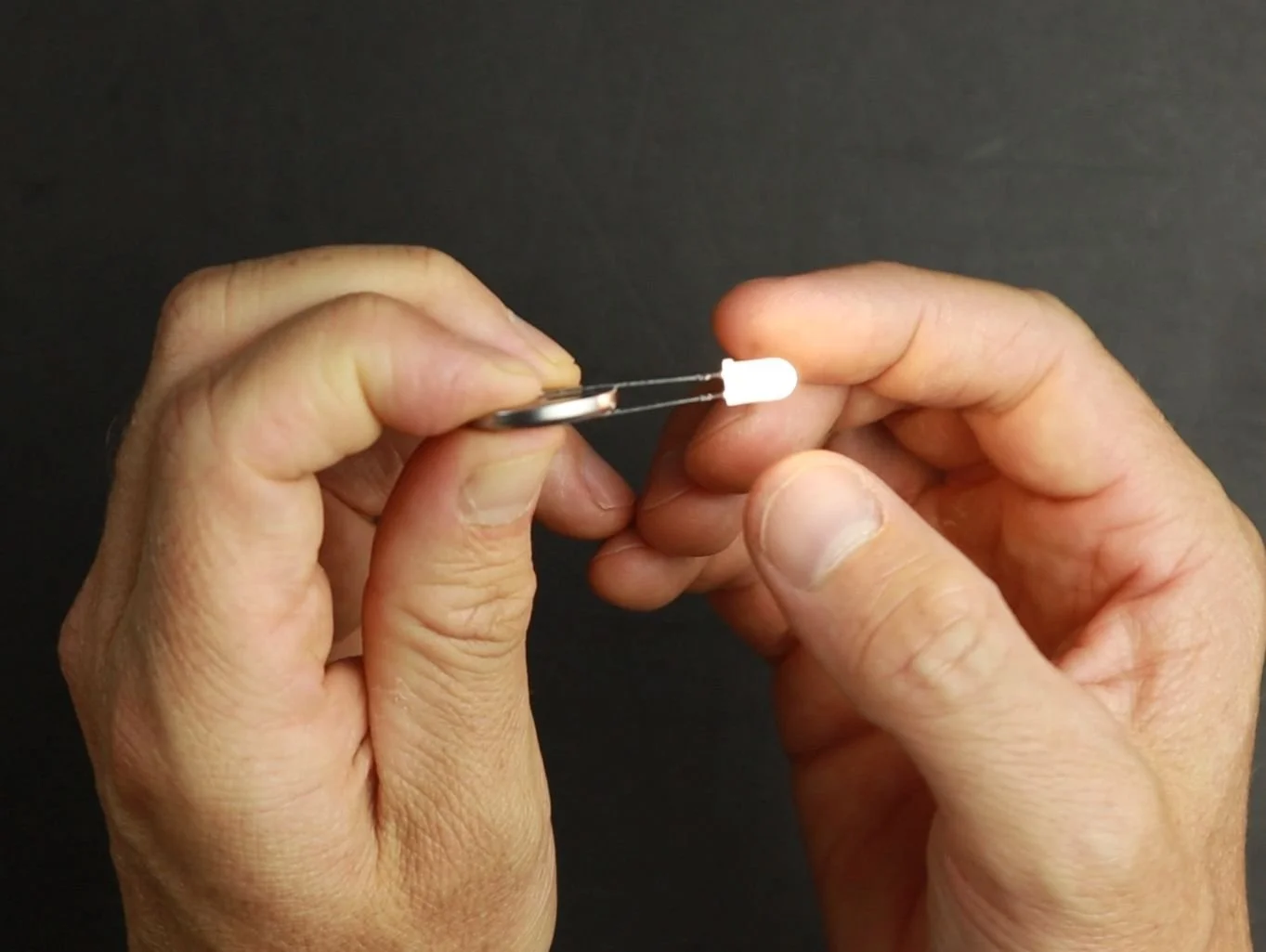 Two hands holding a button cell and LED. The LED is put onto the button cell which lights the LED up.