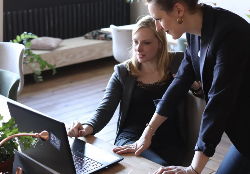 An image of two wome sitting in front of a laptop in an office setting