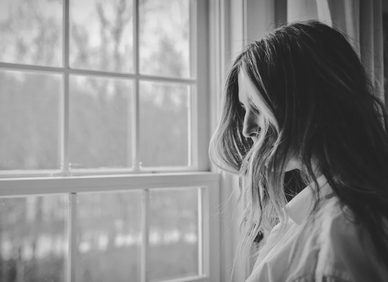 A black and white image of a woman standing in front of a window