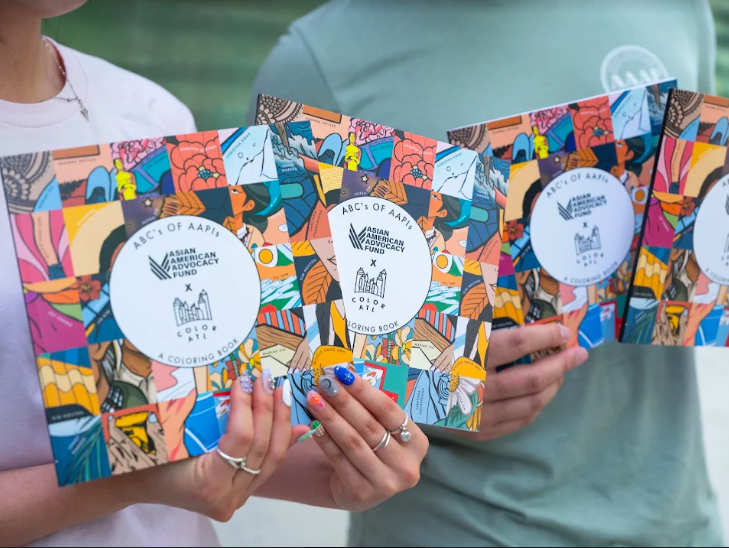 Two people hold up four books to the camera, the title of which reads "ABCs of AAPIs: A Coloring Book" with a collage of illustrations.