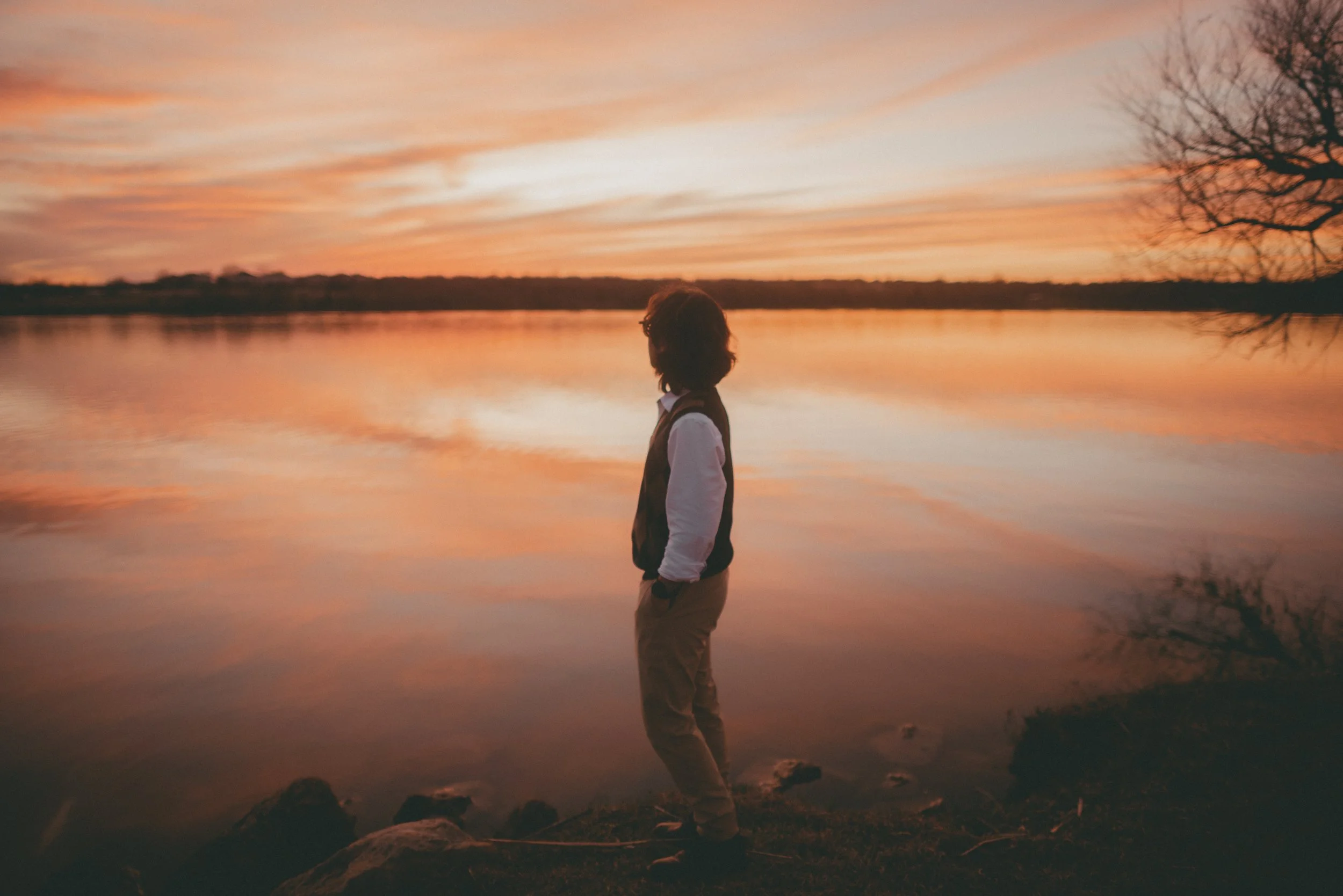 Silhouette of a person standing by a lake during sunset with a colorful sky and trees.