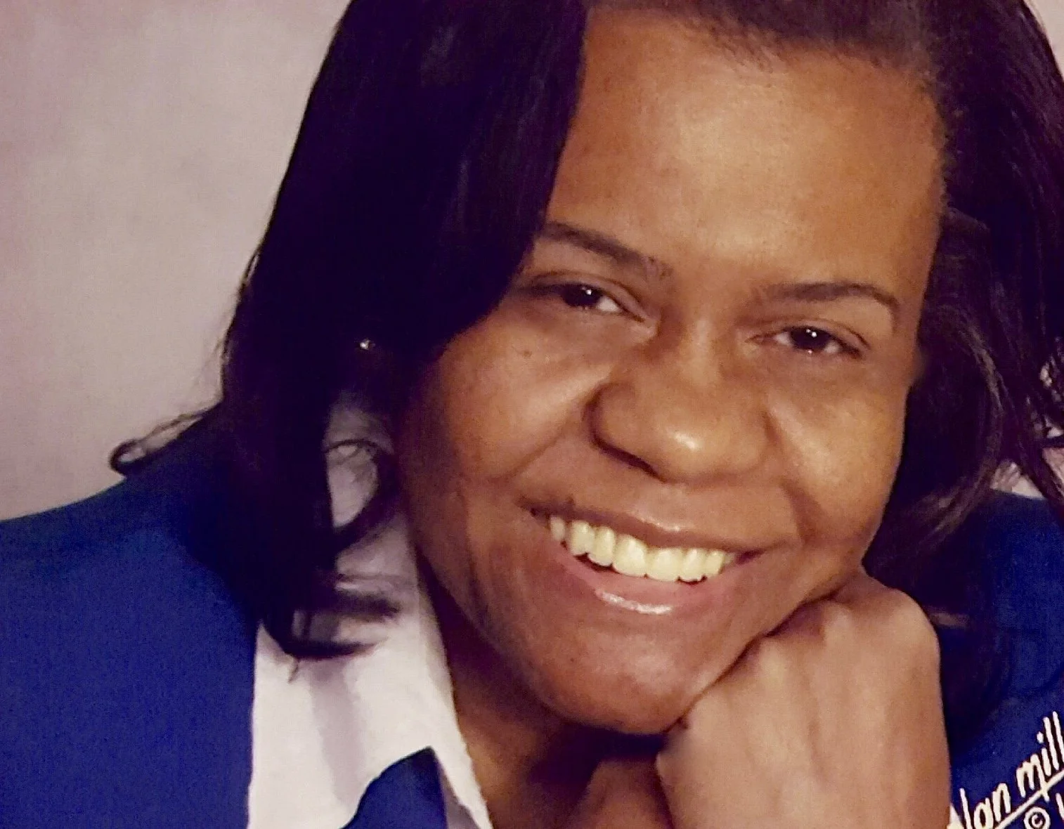 Close-up photo of a woman with dark hair, smiling and resting her chin on her hand.
