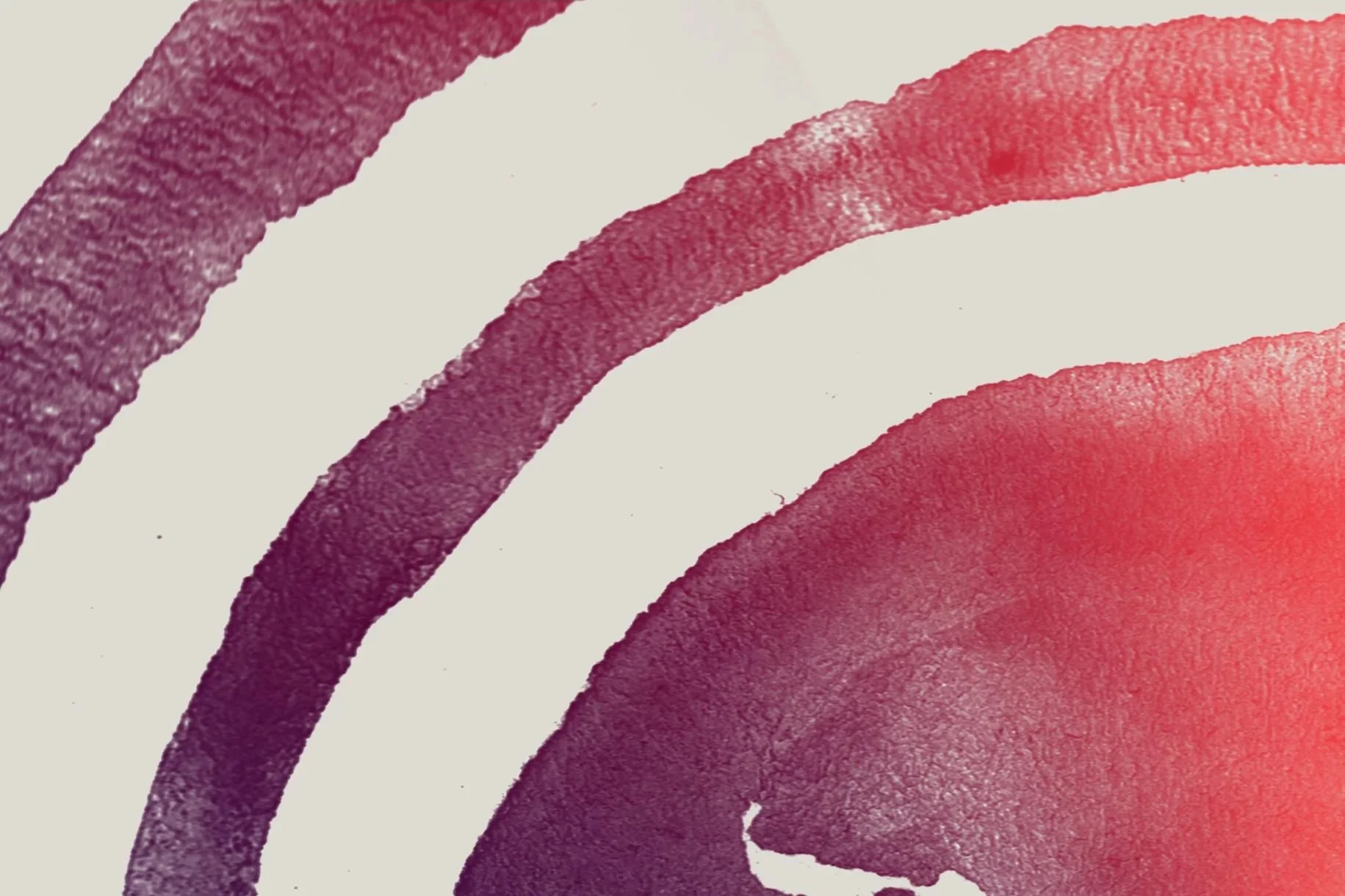 Close-up view of watercolor paint streaks in shades of pink, purple, and red on textured paper