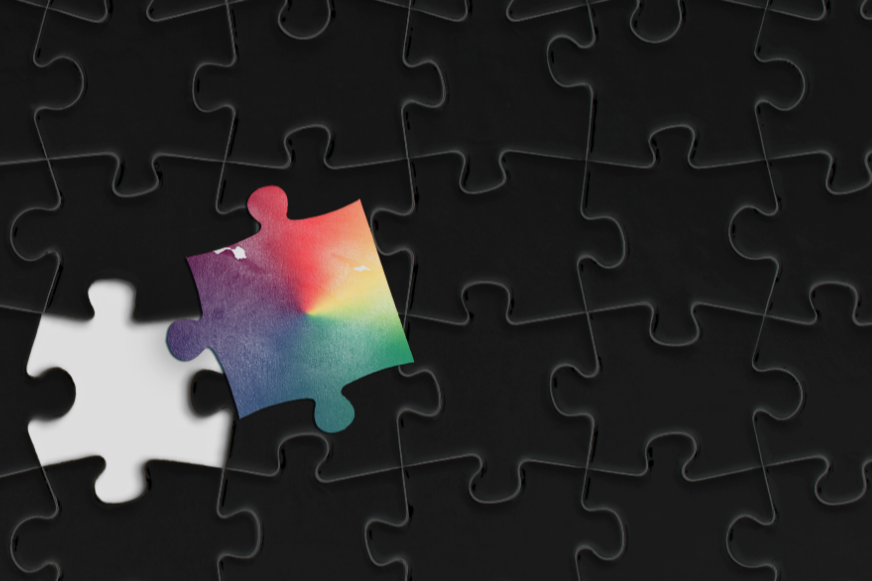 Black puzzle with a missing piece and a rainbow-colored puzzle piece near it.