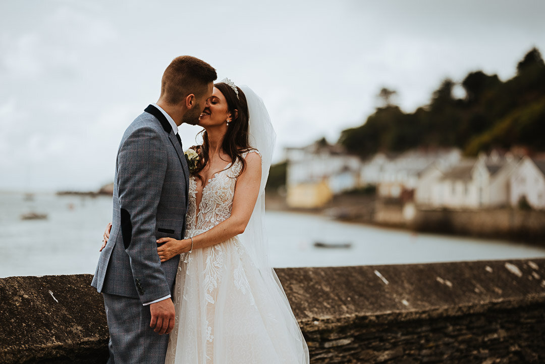 bride and groom share a kiss next to the sea wall in Aberdyfi