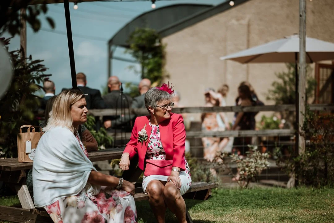 Wedding guests are sitting on the bench outside having a drink