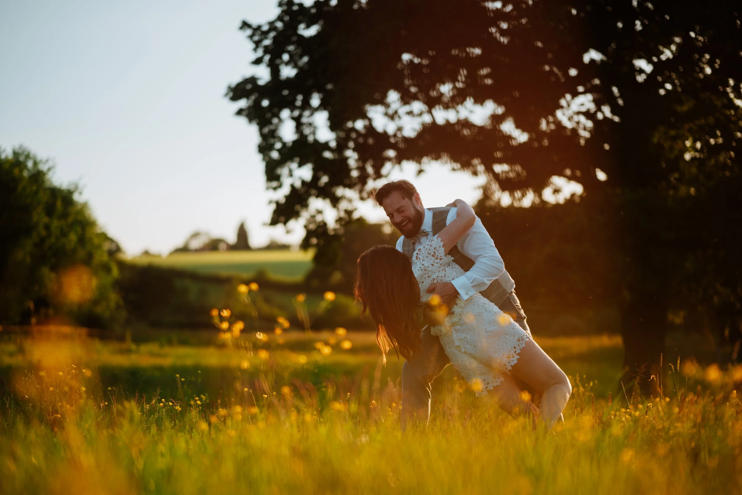 bride and groom are on a field during golden hour and the groom has dipped her whilst they pretend to dance