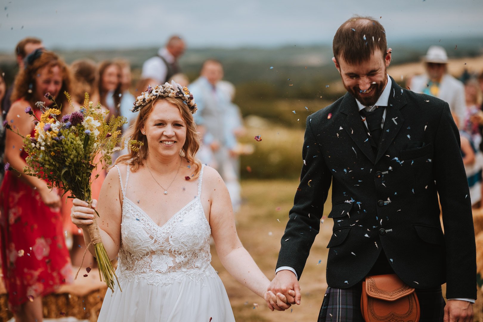Confetting being thrown on a bride and groom as they walk down the isle on a field