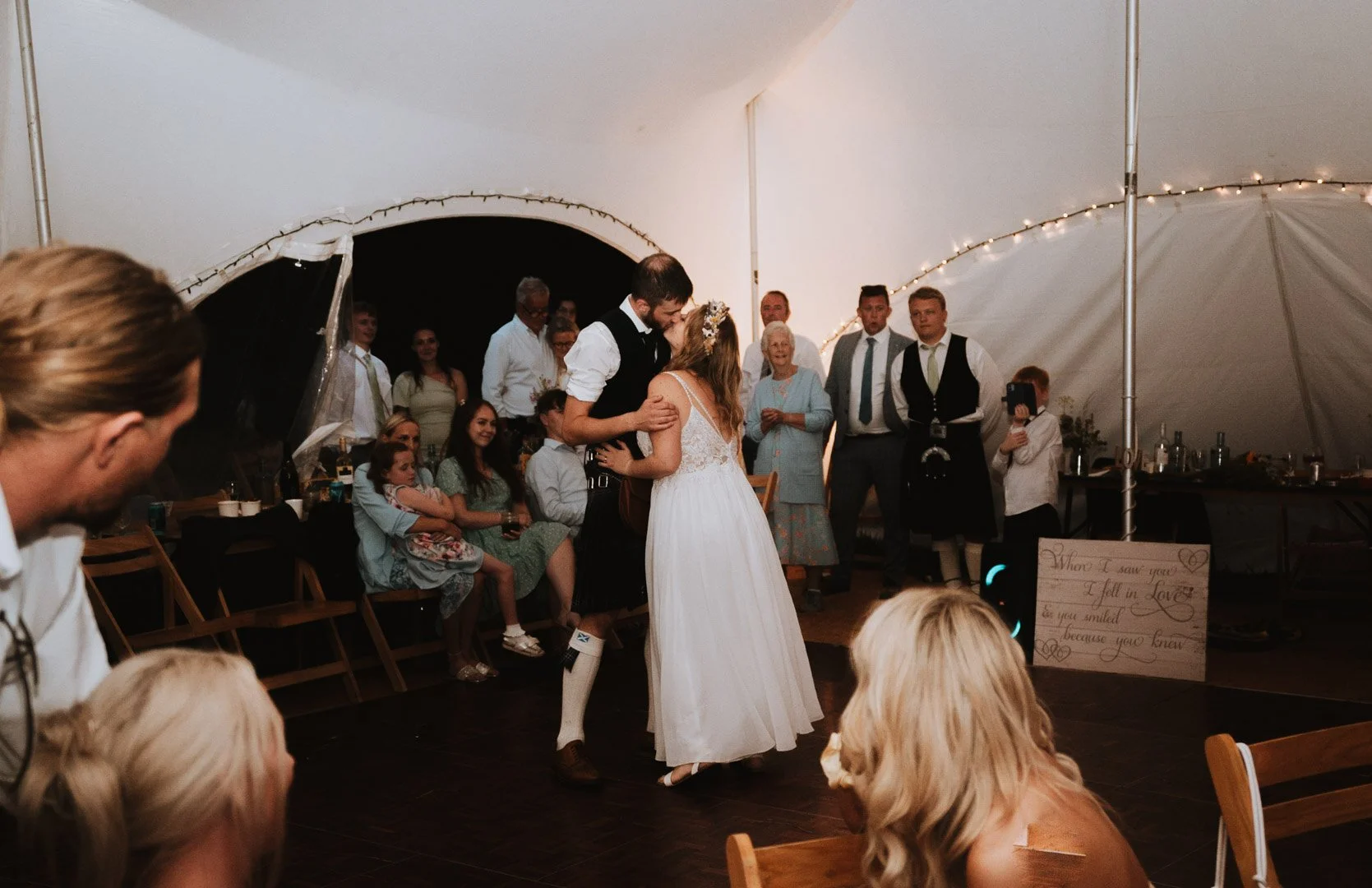 A bride and groom share a kiss during their first dance, inside a marquee tent on a camp site in Somerset, being watched by their guests