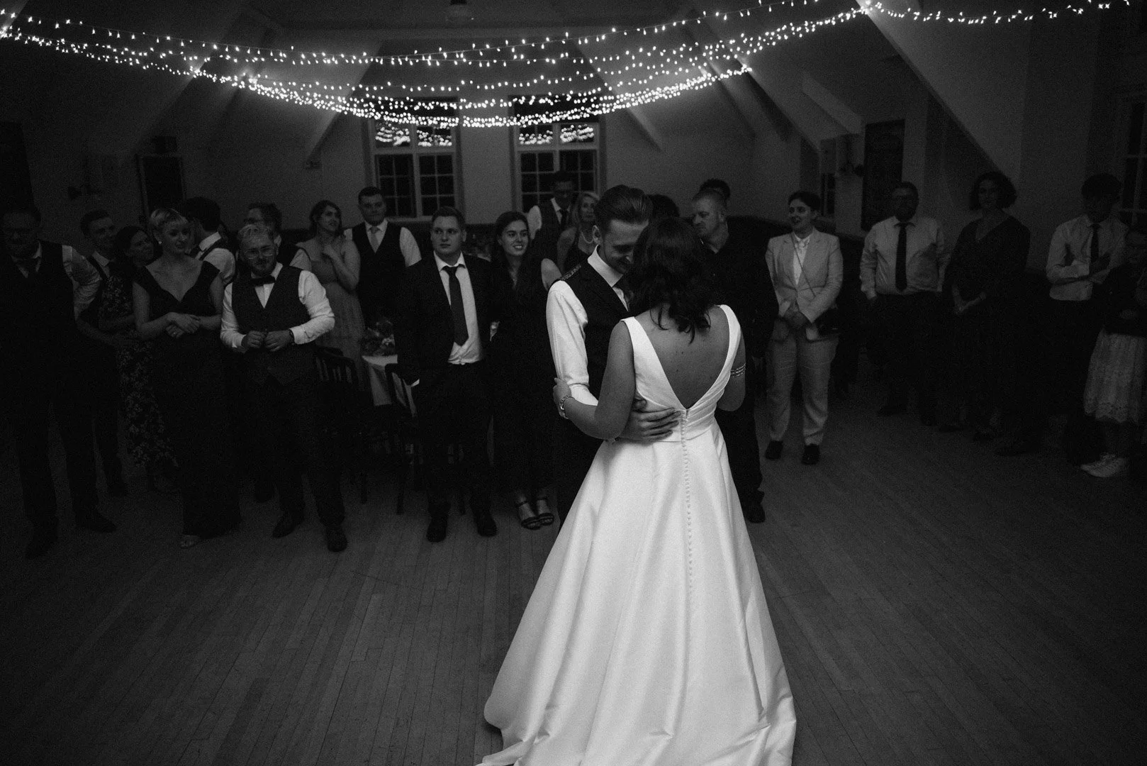 black and white image of a bride and groom sharing their first dance in front of observant wedding guests at St Fagans Museum in Cardiff