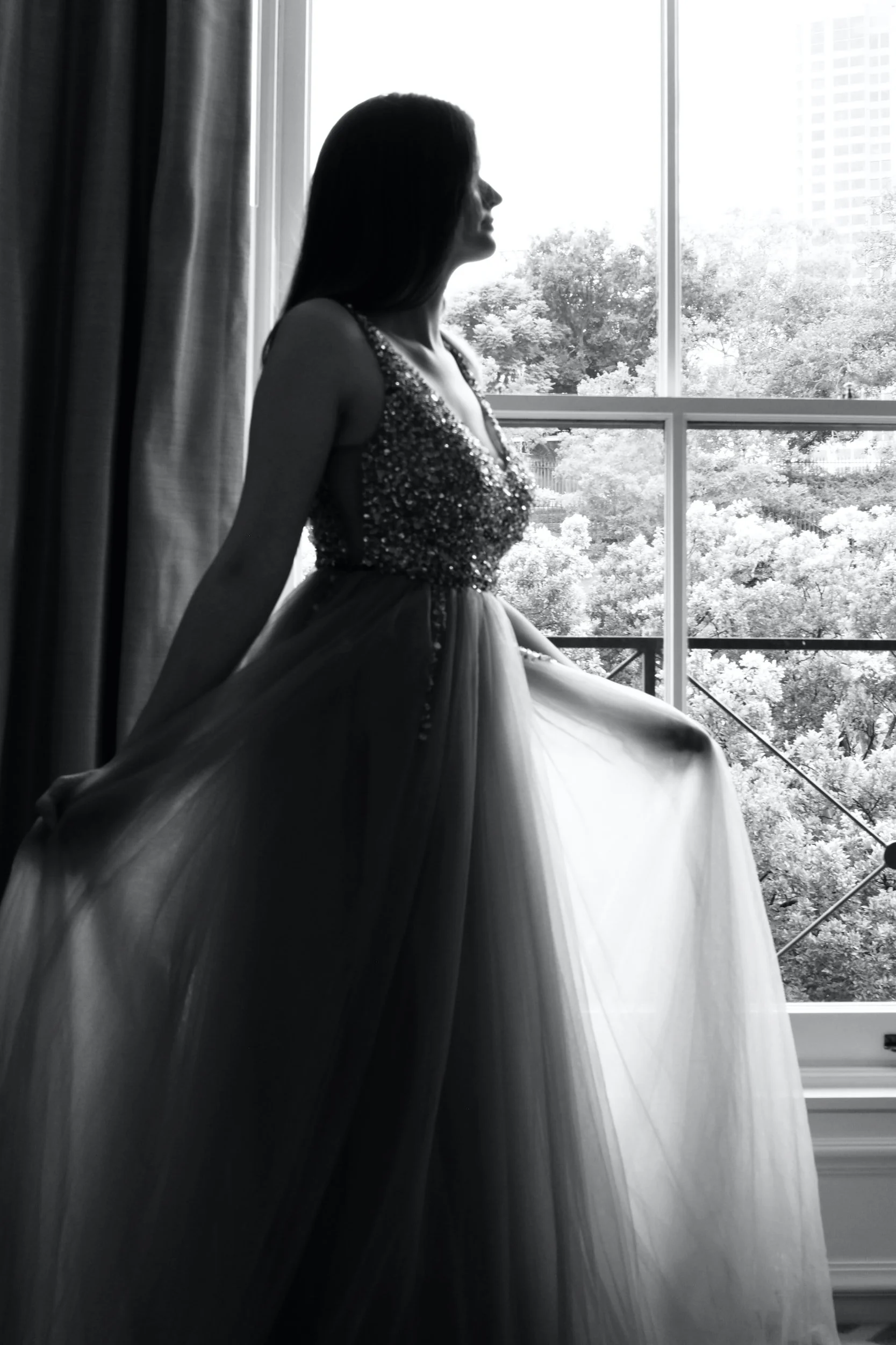 black and white photo of bride in a wedding dress stood by a window