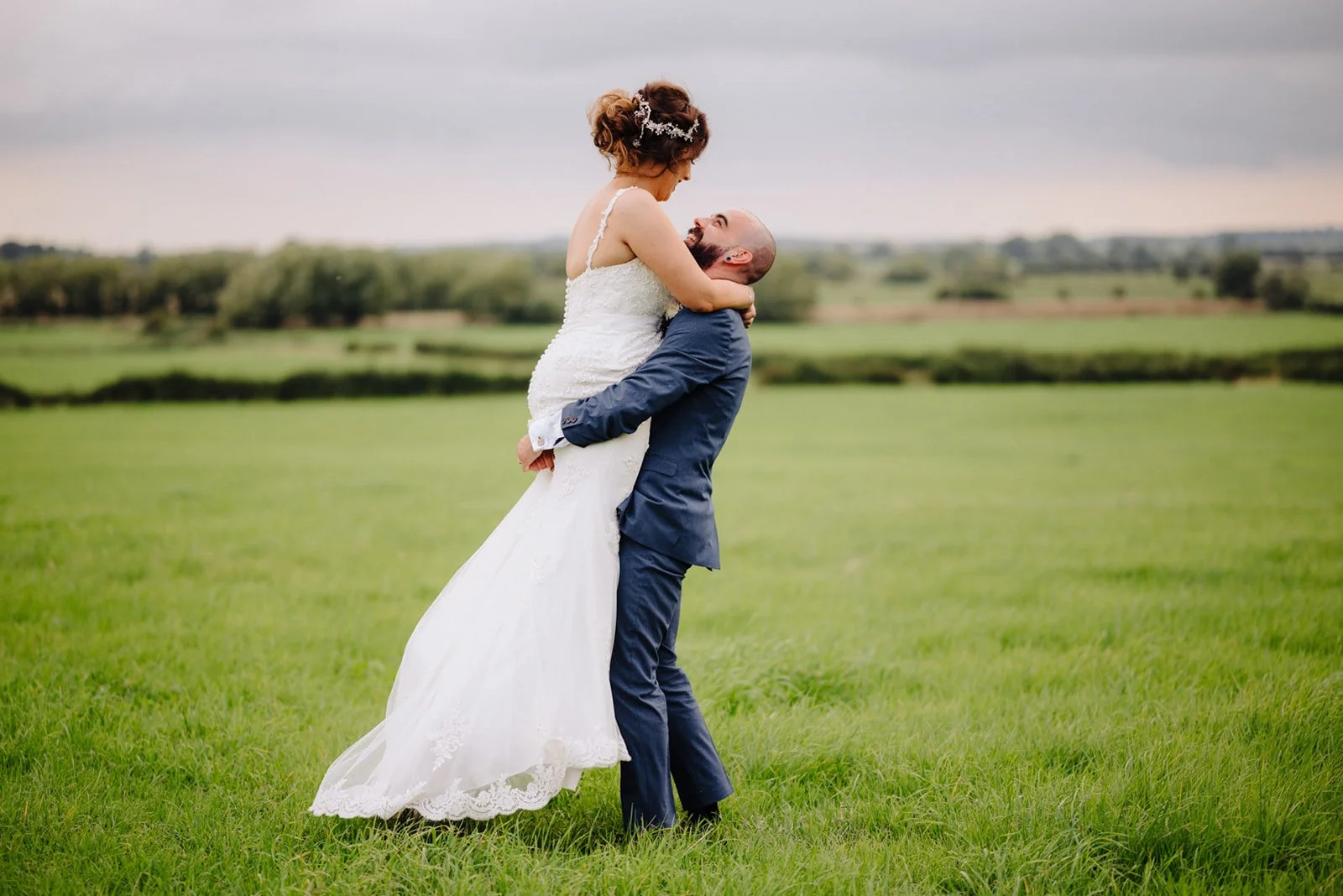 groom picking up his bride and twirling her around on a field at the Dairy House Farm in Somerset