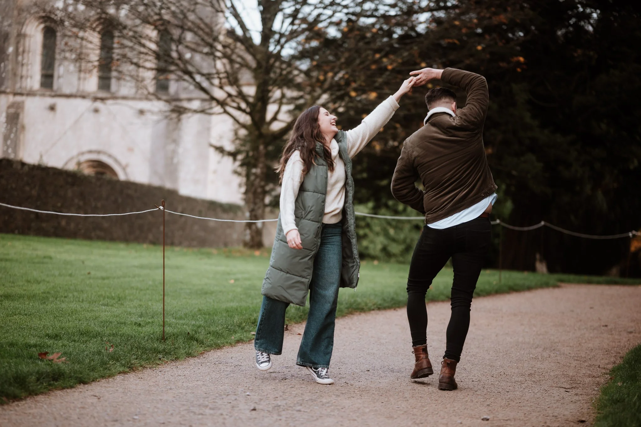 man and woman are fooling around and the man twirls his fiance around as they share a stroll in Margam Park near Swansea