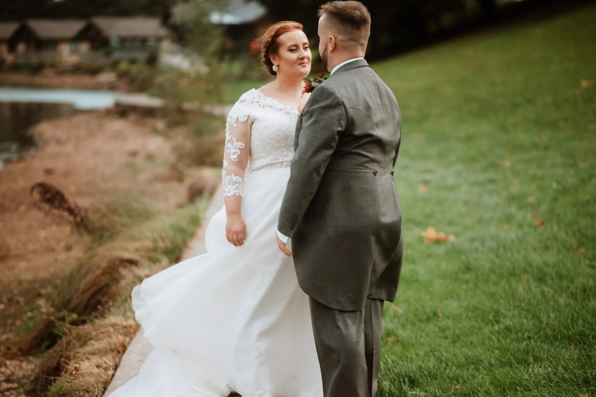 a bride and groom are facing each other and smiling as they stand next to the lake at Canada Lodge in Cardiff