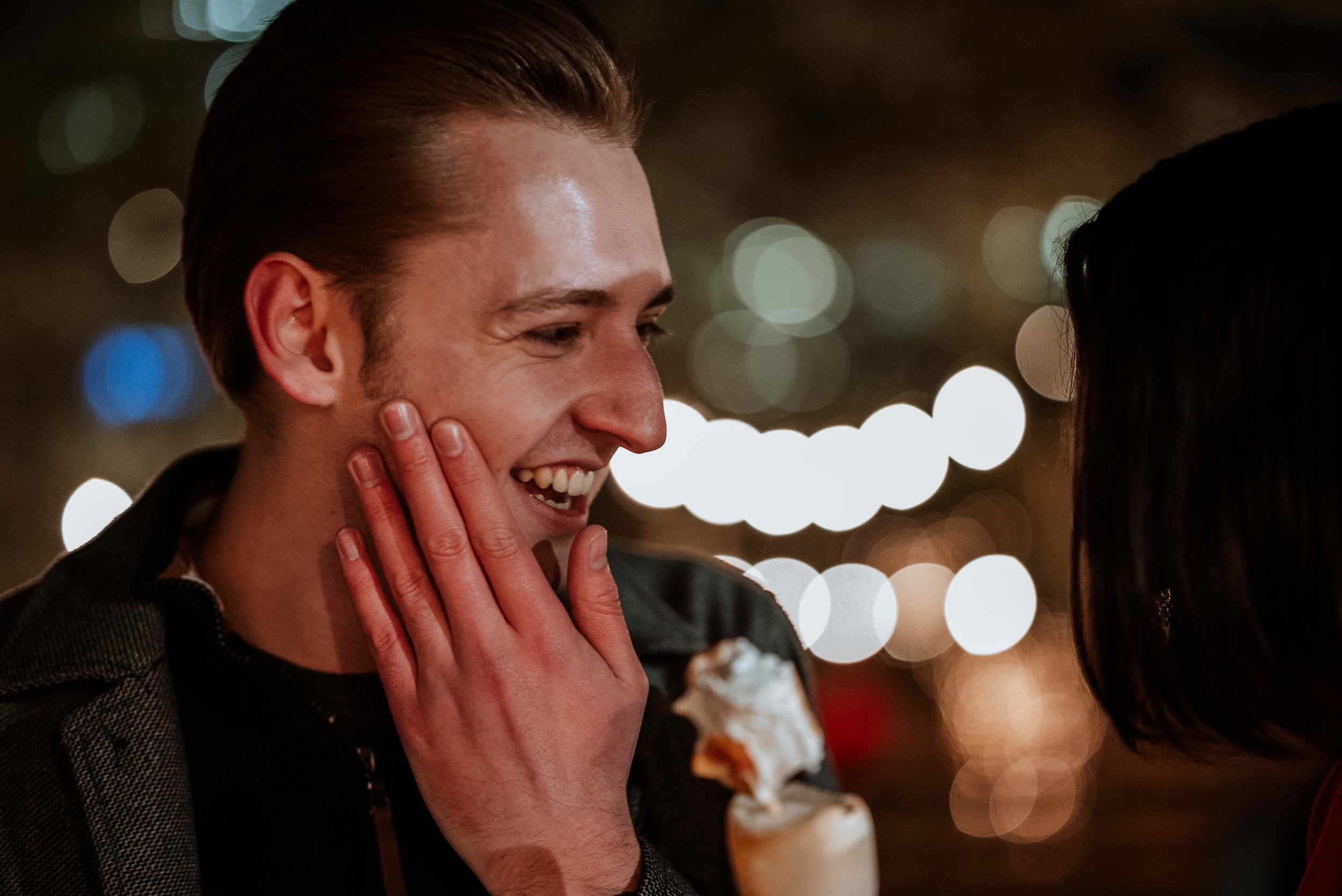 man laughing whilst stroking his own face in amusement, bokeh Christmas lights in the background
