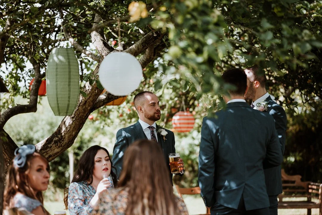 The groomsmen enjoy a pint and a conversation on a sunny wedding day in the orchard garden