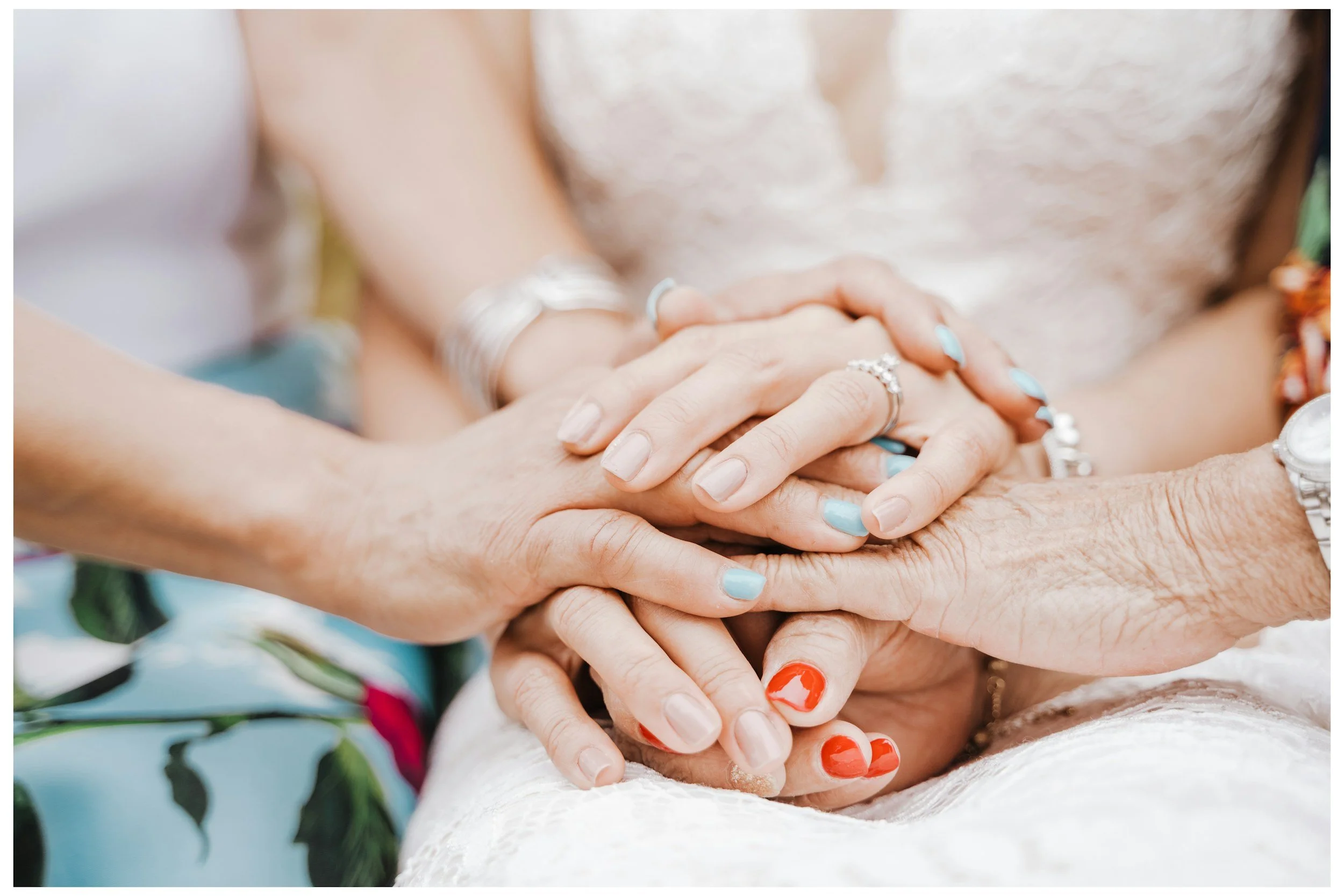 Bride's hands entwined with her mother and grandmother's hands on her wedding day.