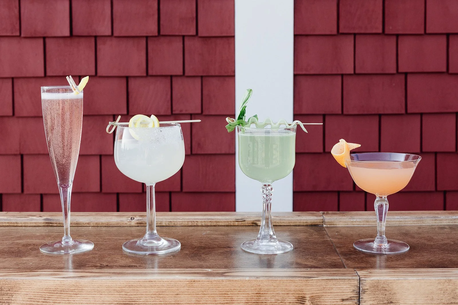 Display of fancy wedding cocktails on a handmade wooden bar top outside of a wedding barn.