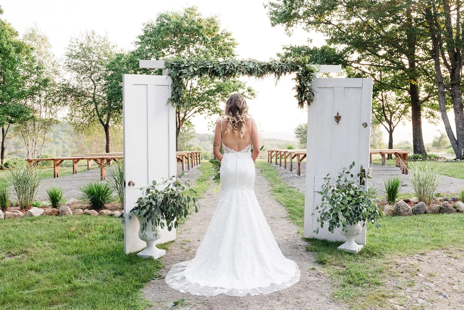 Bride stands between two white doors as she begins her walk down the aisle at New Hampshire wedding venue in summer adorned with greenery.