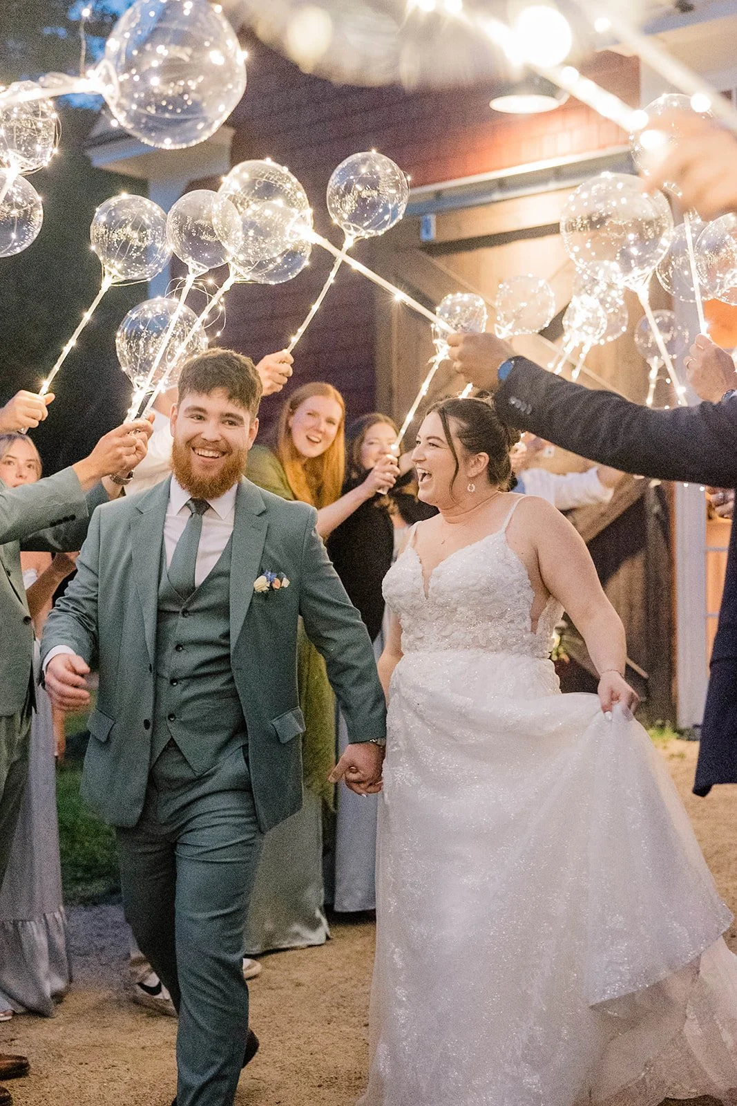 Bride and groom smile as they walk through a tunnel of lighted balloons during their garden wedding send off.