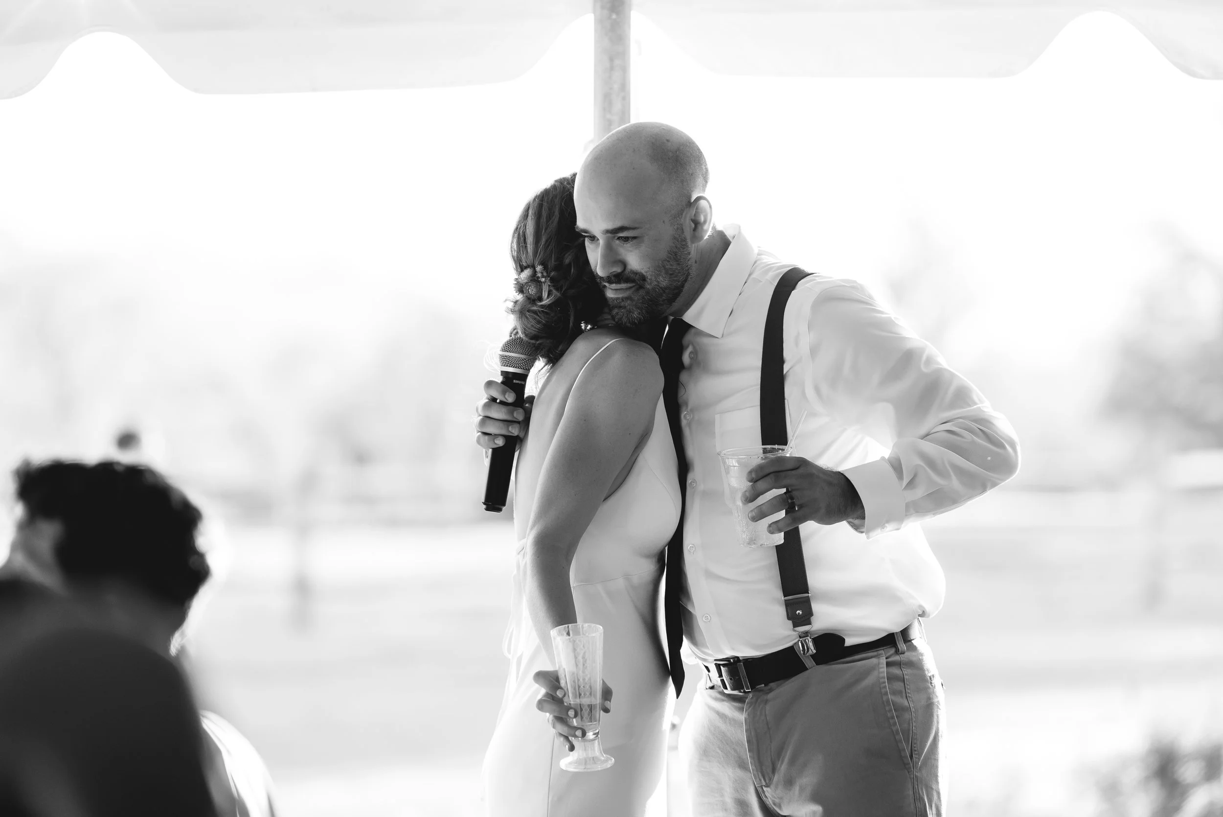 Groomsman and bride embrace after speech at wedding.
