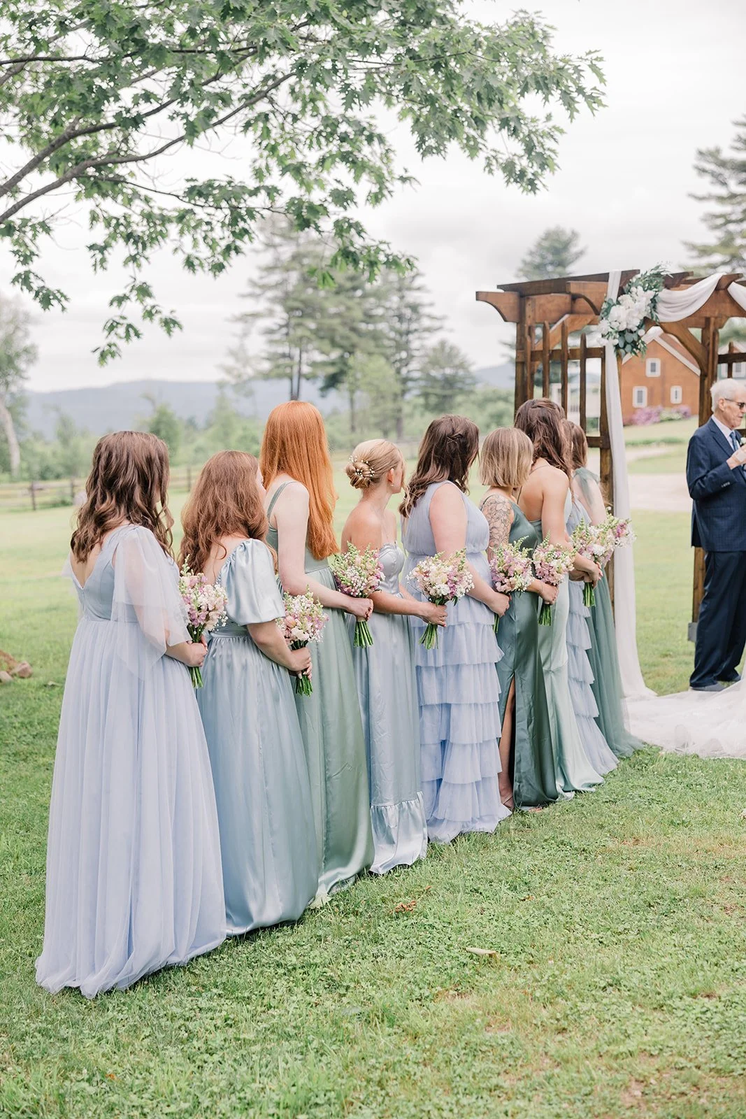 Bridesmaids wearing different shades of light blue and green look on at garden wedding ceremony.