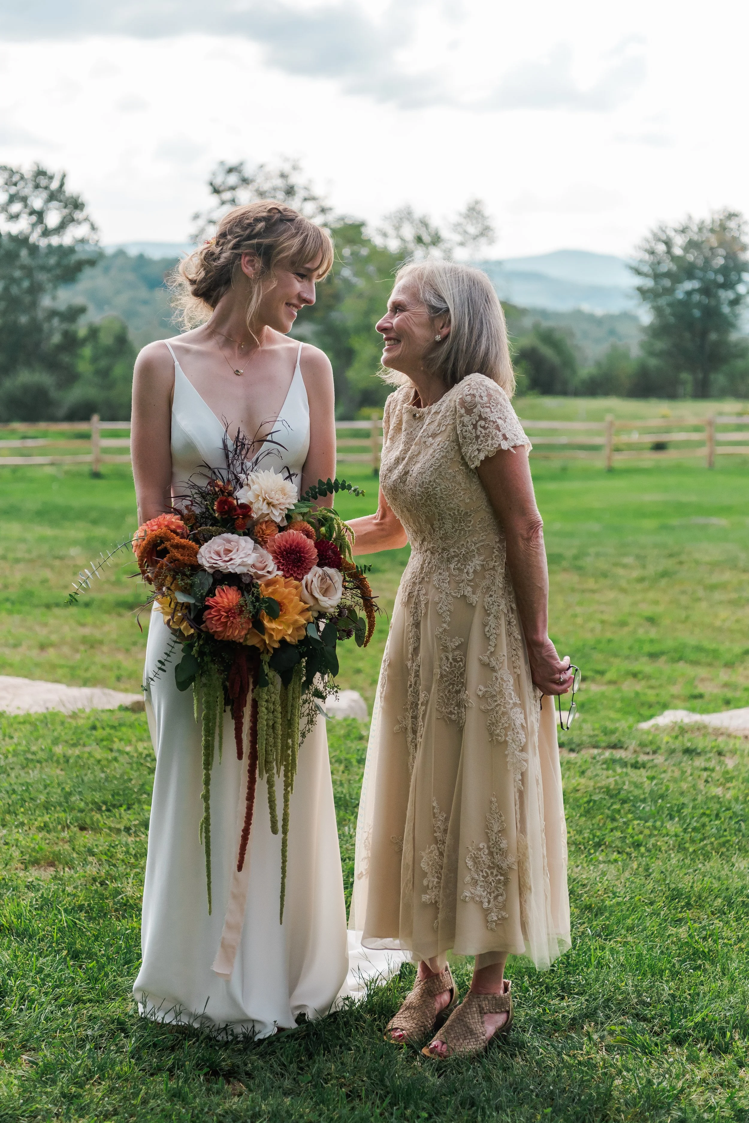 Bride and Mom smile at each other on wedding day with mountains in the background.