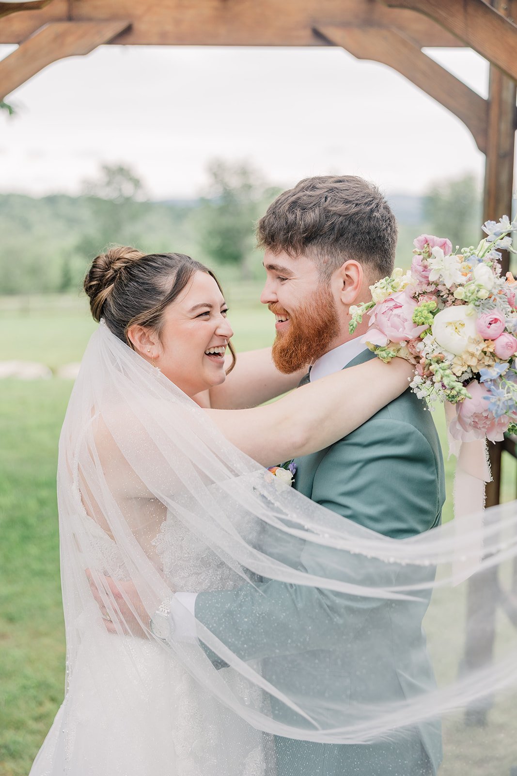 Bride and groom embrace and smile while wrapped in the bride's long sparkly veil at their garden wedding ceremony.
