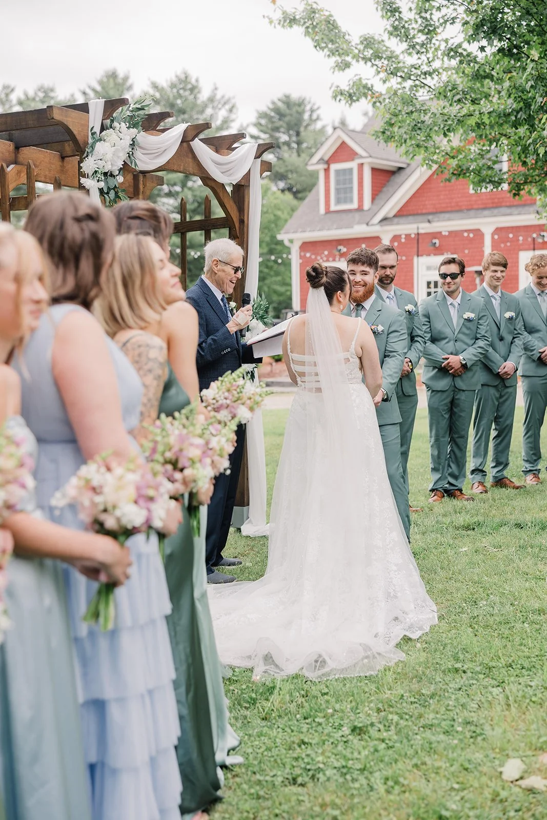 Bridesmaids laugh and the officiant smiles during an outdoor garden wedding ceremony.