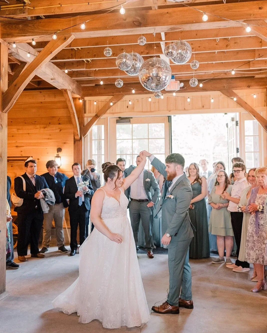 Bride and Groom share a first dance surrounded by loved ones under a disco ball chandelier.
