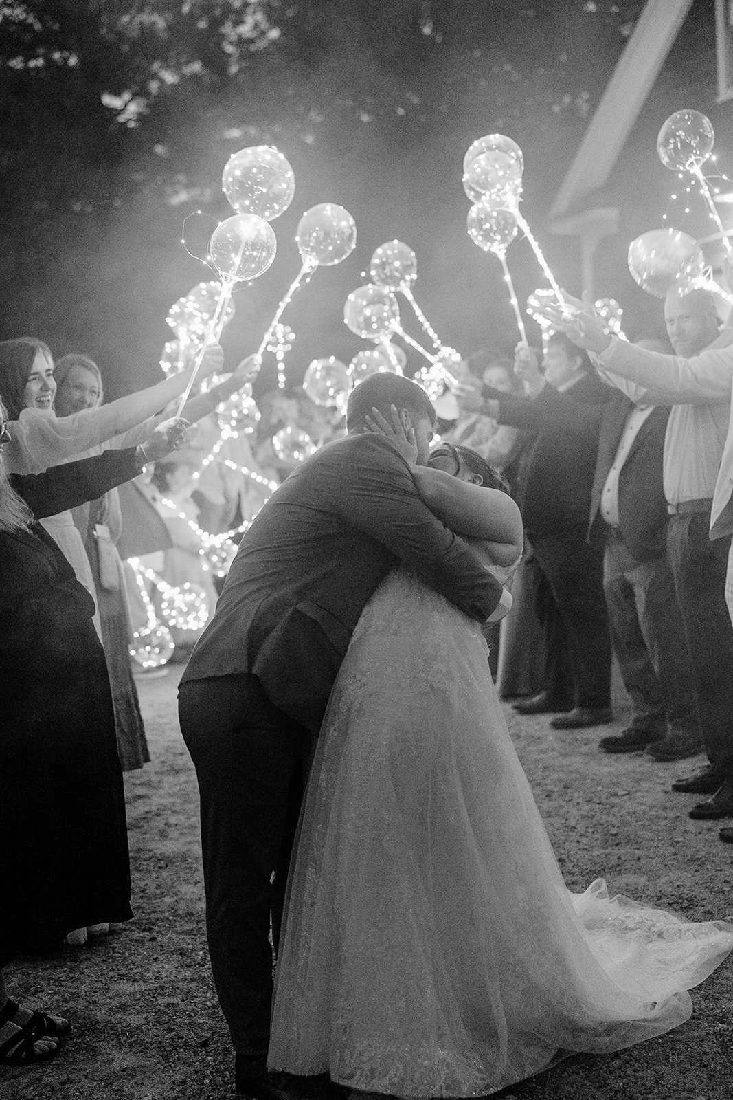 Bride and groom share a kiss between a runway of lighted balloons during their garden wedding send off.
