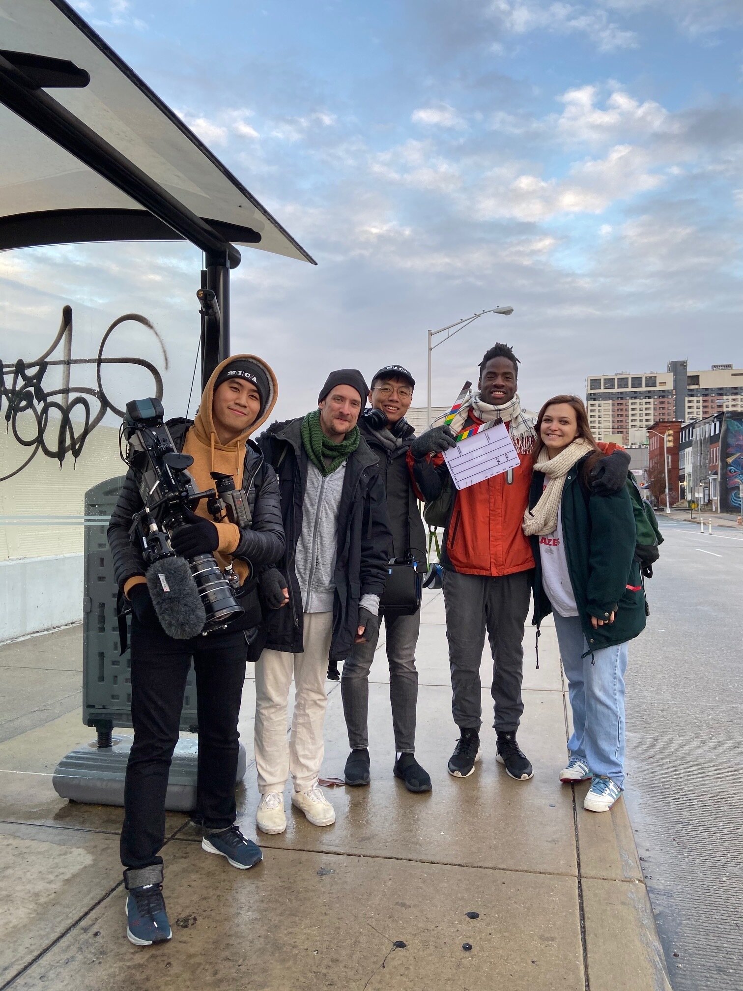 Film crew posing behind the scenes at a bus stop.