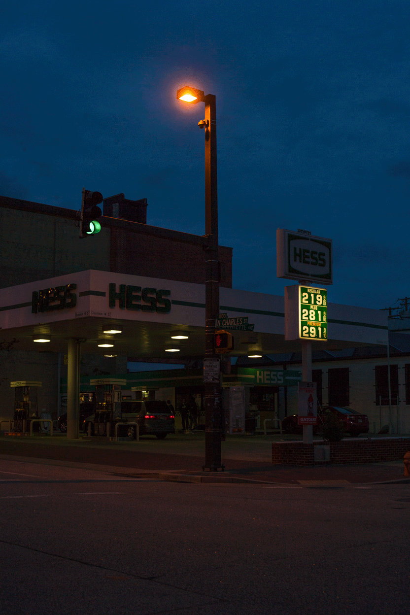 Street lights, a gas station sign, and tail lamps flicker in sync at an empty road.