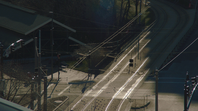 Silhouettes of several cars and a pedestrian cross train tracks.