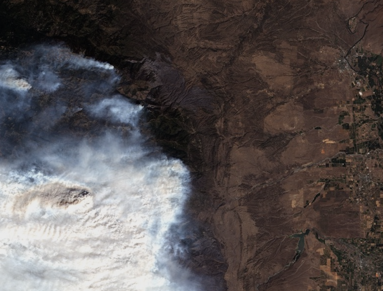 Satellite image of a wildfire with smoke over a mountainous and rural landscape