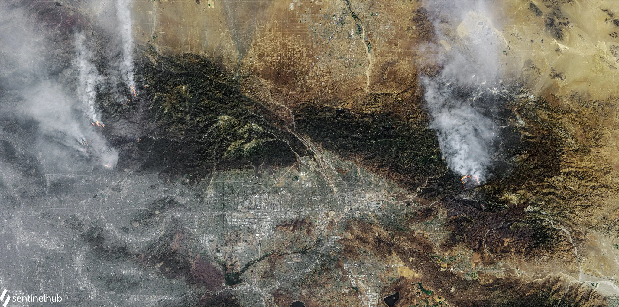 Satellite view of wildfires in mountainous terrain, showing smoke plumes and fire hotspots.