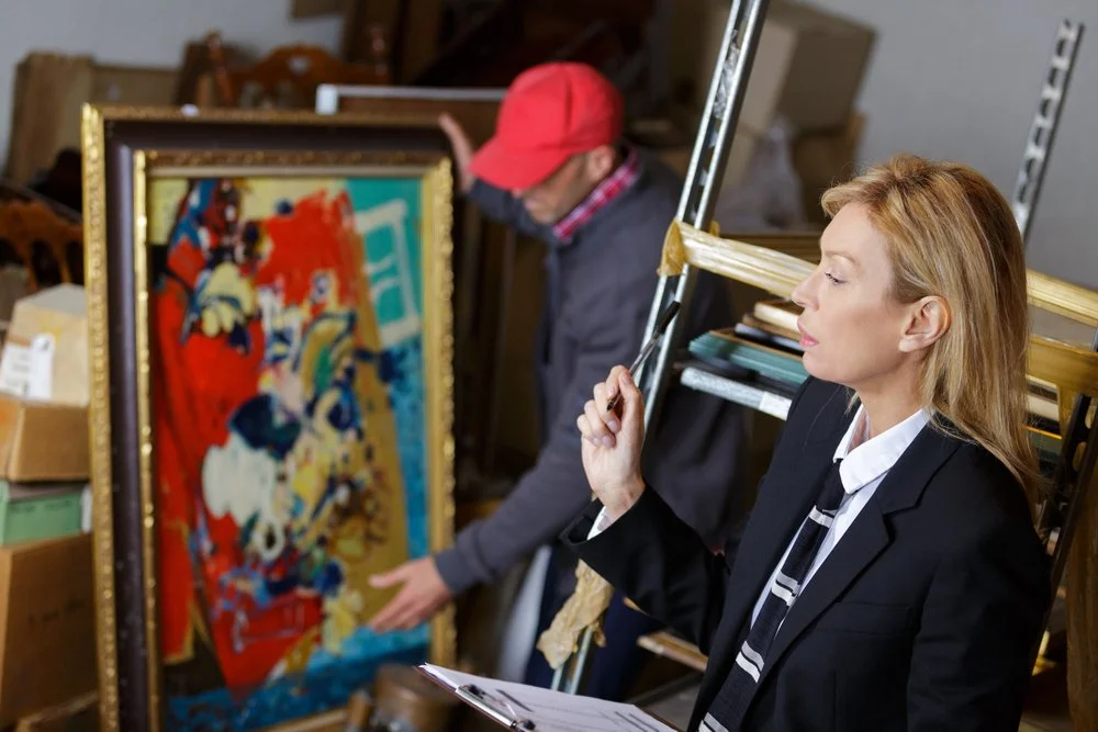 Two art gallery staff members examining a colorful abstract painting in storage.