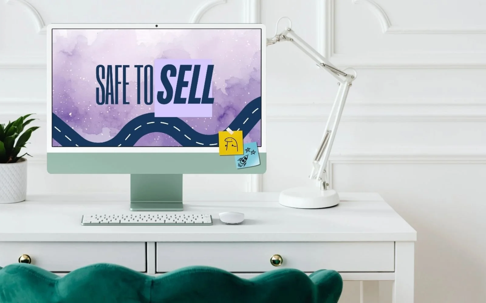 A white computer desk with a white computer monitor displaying a purple watercolor background with the words "Safe to Sell" in bold, along with a desk lamp, a white keyboard, a white mouse, a small potted plant, and sticky notes with drawings.