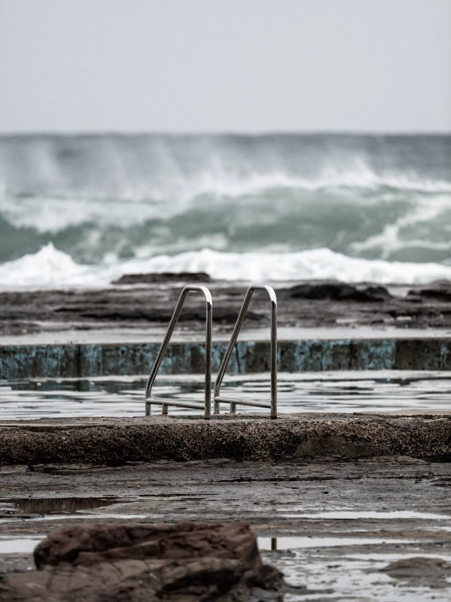 An image of the handrails from pool level at Coledale with a decent wave breaking in the background