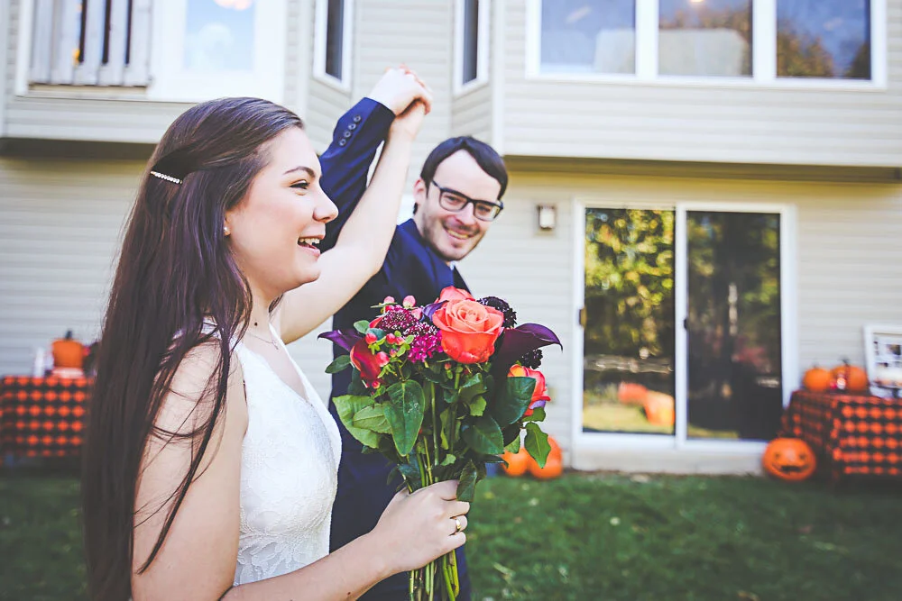 A wedding couple throw their hands up in the air to celebrate their marriage in their backyard Halloween ceremony.